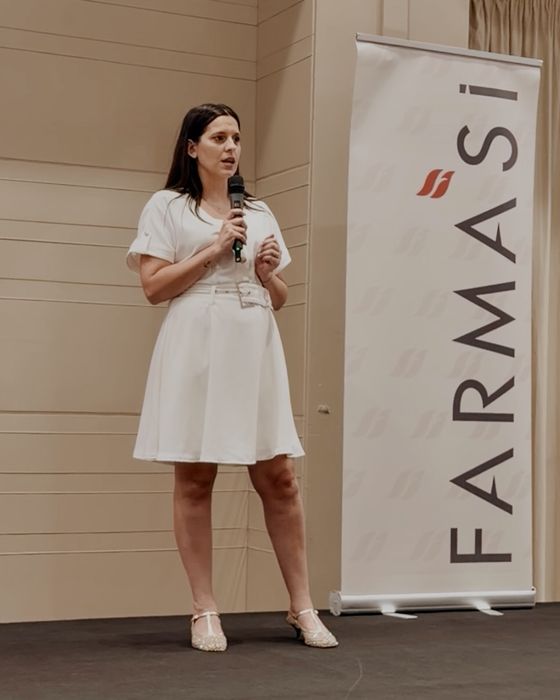 Vanessa Cesarano parla al microfono su un palco, accanto a un roll-up con il logo Farmasi.